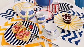 Una mesa de comedor con mantel azul y blanco a rayas, un jarrón azul con limones amarillos y diferentes platos y cubiertos.