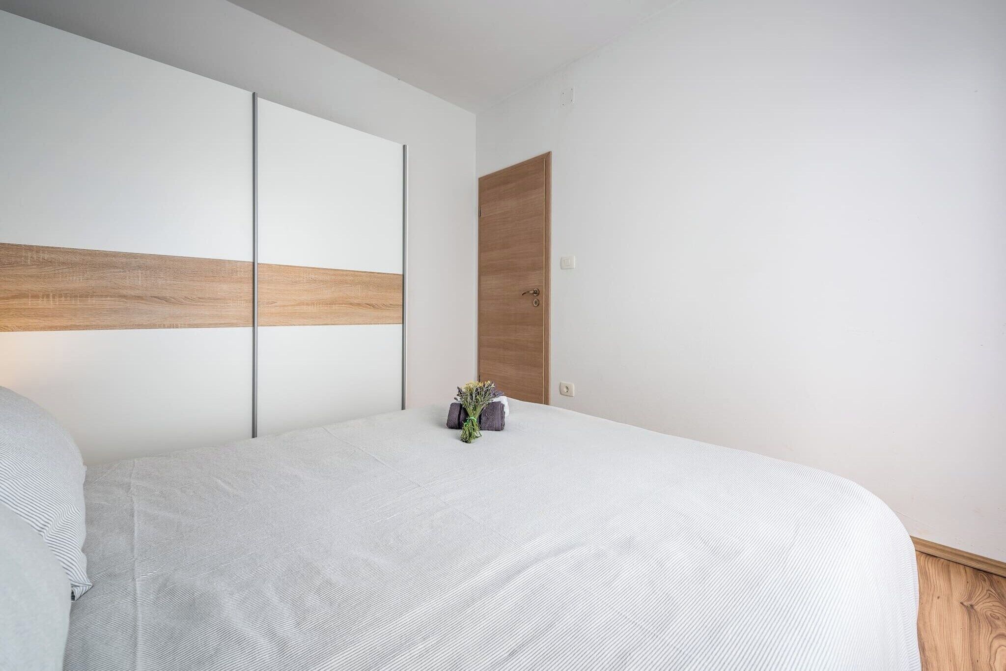 A modern bedroom with a large bed, a wooden headboard, and a small plant on the nightstand.
