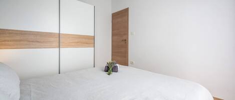 A modern bedroom with a large bed, a wooden headboard, and a small plant on the nightstand.