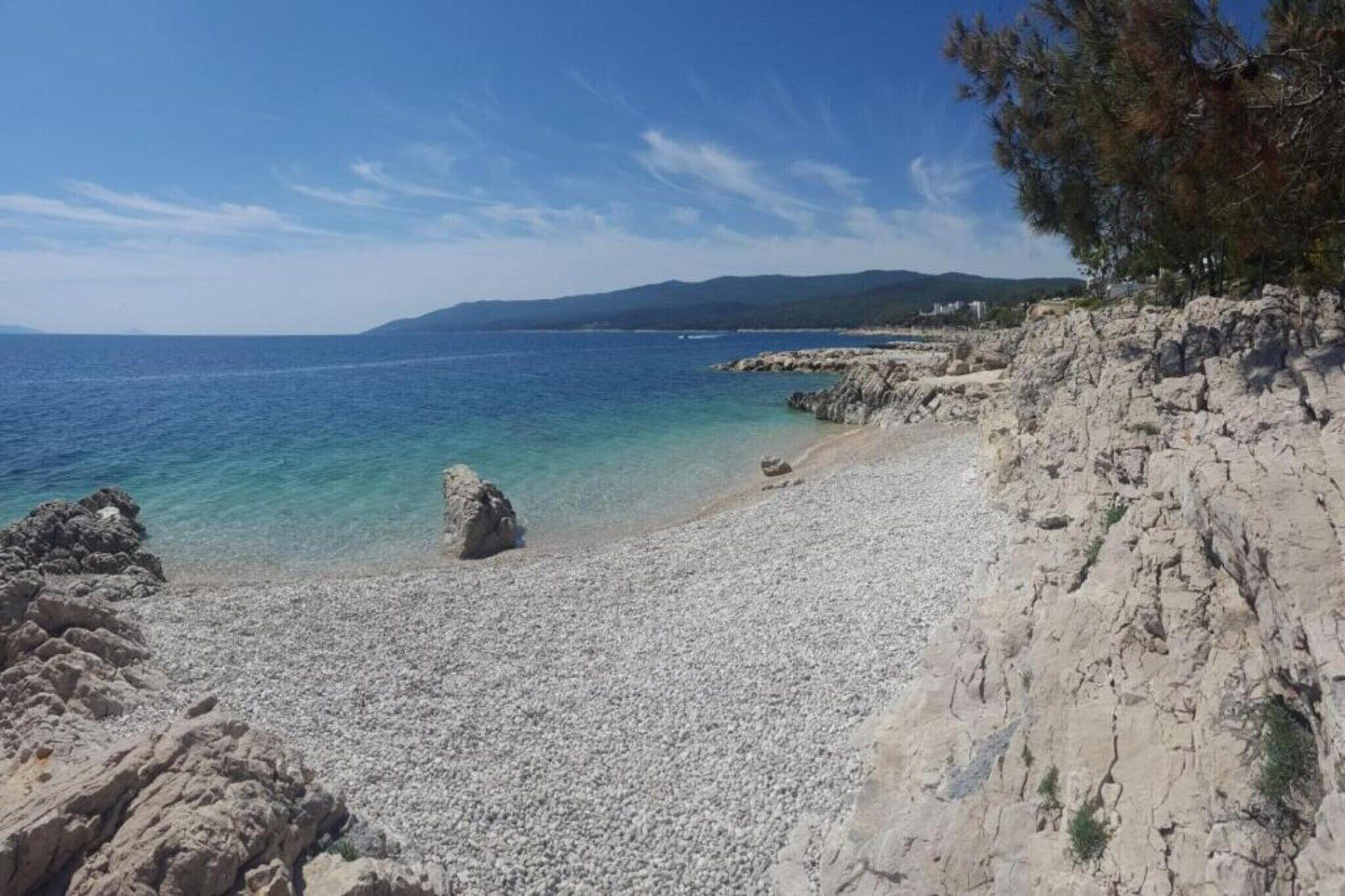 A pebble beach with clear blue water and rocky cliffs.