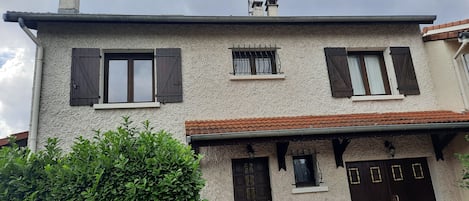 A two-story building with stucco walls, wooden shutters, and a tiled roof.