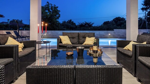 An outdoor seating area with wicker furniture, a glass table, and a pool in the background.