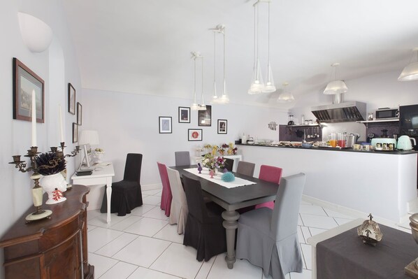 A modern dining area with a long table, chairs, and a kitchen in the background.