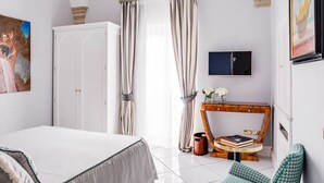 Quarto com uma cama, escrivaninha, cadeira, televisão e um quadro.