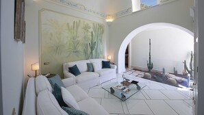 Uma sala de estar espaçosa com um sofá branco, uma mesa de centro de vidro e um grande jardim de cactos visível através de um arco.