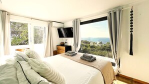 Un dormitorio con cama, televisor, cómoda y vista al mar.
