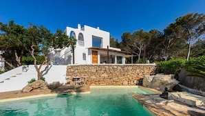 Una villa blanca moderna con muro de piedra y piscina.