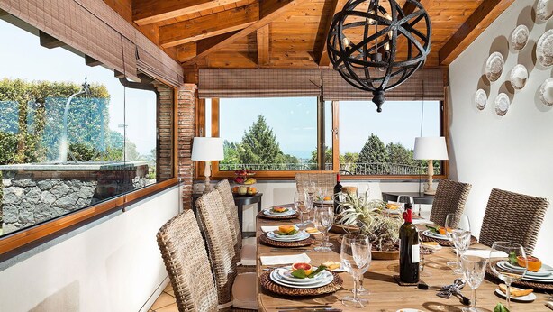 Un comedor con una mesa de madera dispuesta para una comida, sillas de mimbre y vistas al exterior.