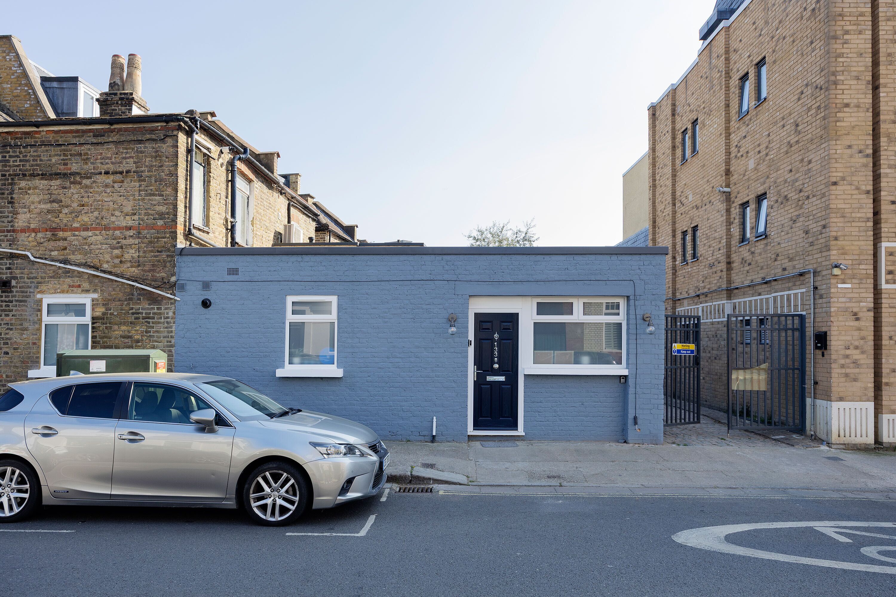 A building with a blue facade, a black door, and a parking space marked with a wheelchair symbol.