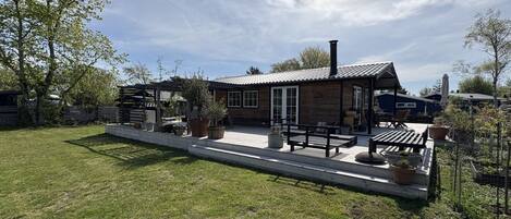 Situated in a serene natural setting, this cabin-style building offers a welcoming outdoor space with a front porch and potted plants.