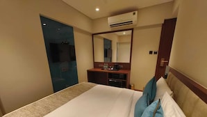 A hotel room with a bed, a desk with a mirror, and an air conditioning unit.
