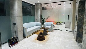 A modern lobby with a marble floor, light blue sofas, and a glass partition.