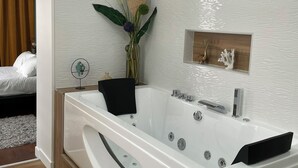 Un baño moderno con una bañera grande, un estante empotrado con objetos decorativos, y piso de madera.