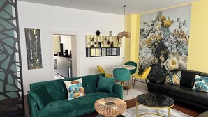 Una sala de estar moderna con un sofá verde, sillas amarillas, una mesa de centro negra y un sofá negro con cojines estampados.