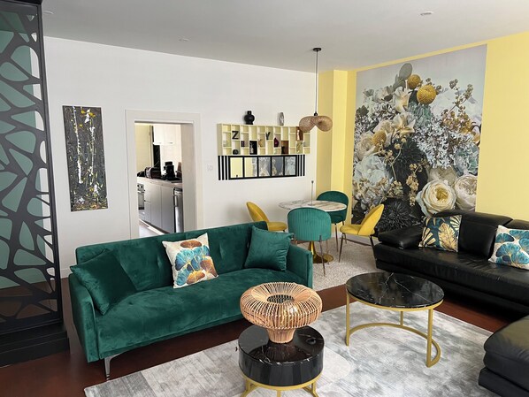 A modern living room with a green sofa, yellow chairs, a black coffee table, and a black sofa with floral cushions.