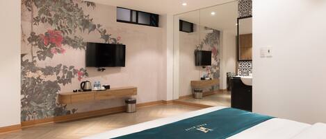A modern hotel room with a large bed, a flat-screen TV mounted on the wall, a wooden nightstand, a mirror, and a bathroom with a sink and toilet.