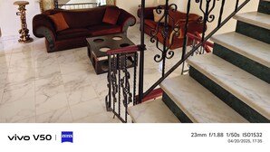 A spacious living room with a red sofa, a coffee table, and a staircase with ornate railings.