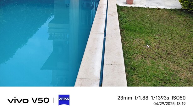 A two-story house with a swimming pool, a balcony with chairs, and a well-maintained garden.