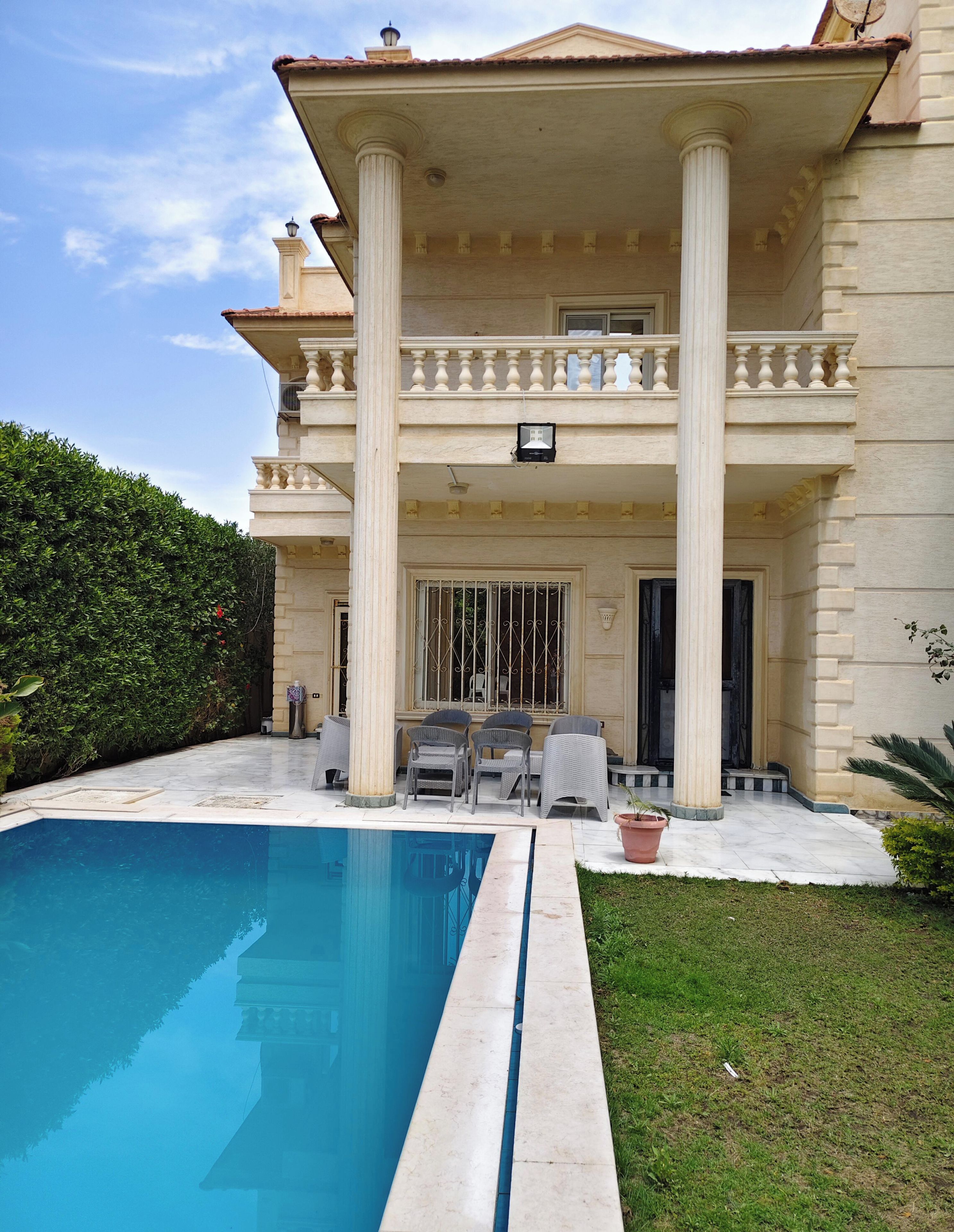 Ein zweistöckiges Haus mit Swimmingpool, einem Balkon mit Stühlen und einem gepflegten Garten.