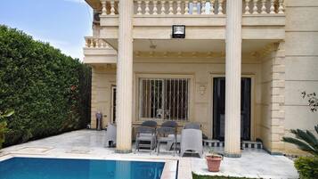 Ein zweistöckiges Haus mit Swimmingpool, einem Balkon mit Stühlen und einem gepflegten Garten.