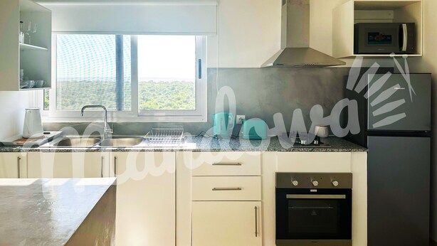 A modern kitchen with white cabinetry, a built-in oven, a microwave, and a window with a view of greenery.