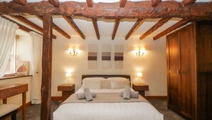 Une chambre avec un plafond en bois, un lit recouvert de draps blancs, deux tables de chevet avec des lampes et une armoire en bois.