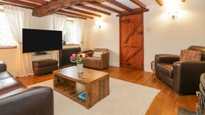 Un salon chaleureux avec un plafond en bois, un téléviseur, des canapés en cuir, une table basse ornée de fleurs et une porte en bois rustique.