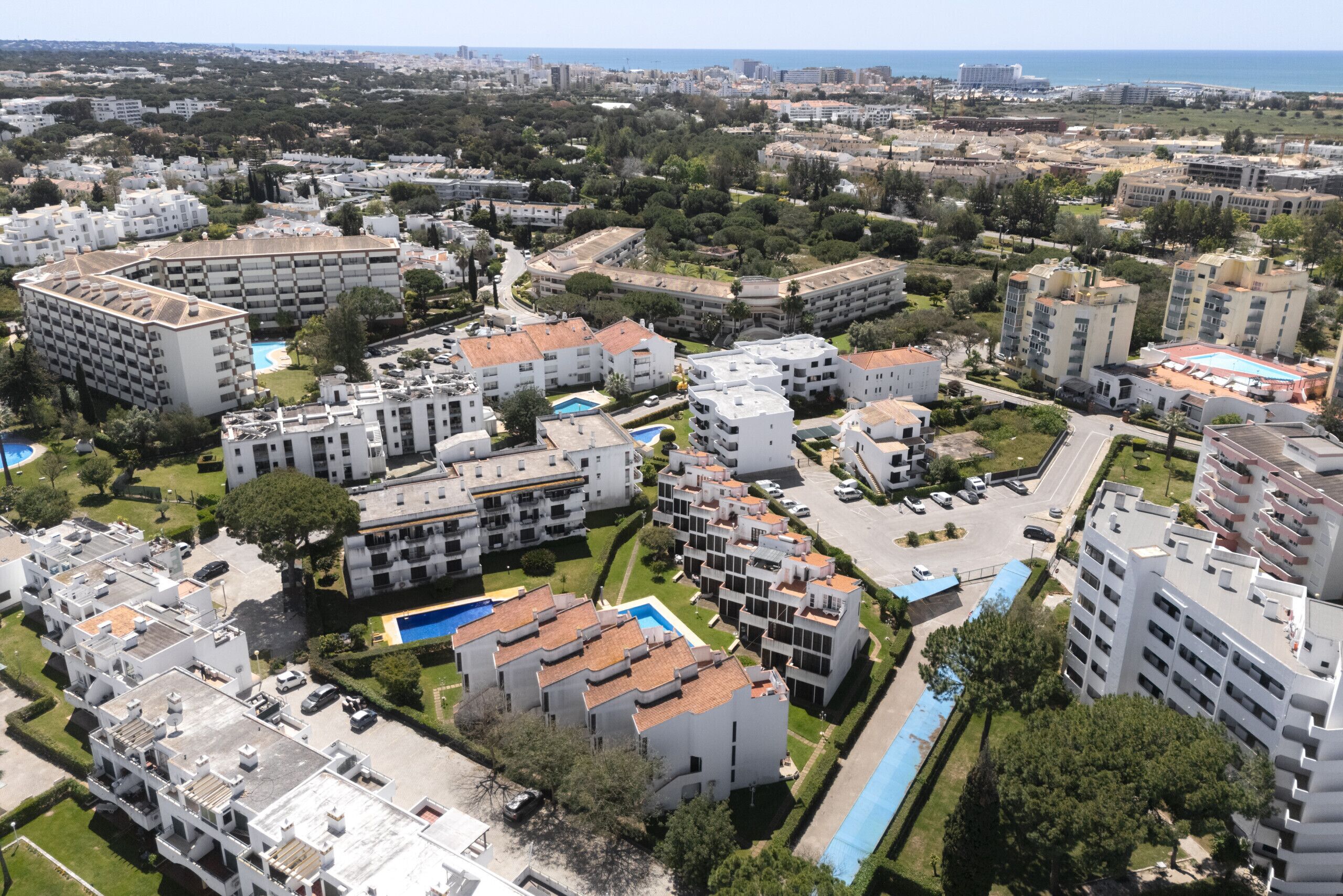 Vista aérea de un área residencial con varios edificios de apartamentos, zonas verdes y una piscina.