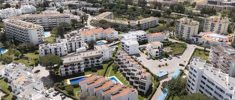 Vista aérea de un área residencial con varios edificios de apartamentos, zonas verdes y una piscina.