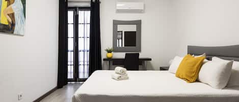 A hotel room with a bed, a desk, a chair, a mirror, and an air conditioning unit.