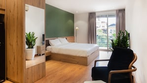 Een moderne slaapkamer met een houten bed, nachtkastje, een potplant, een stoel en een groot raam met gordijnen.
