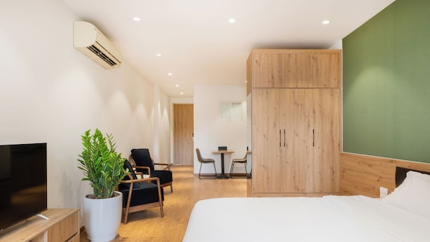 Een moderne hotelkamer met een groot bed, een televisie, een kamerplant en een houten garderobe.