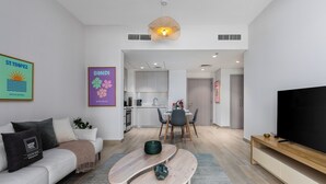A modern living room with a sofa, coffee table, and TV stand. There is a kitchen area in the background with a dining table and chairs. - Maison Privee - Relaxed Yas Island Living Near ALL Attractions (Abu Dhabi)