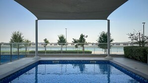 A swimming pool with a tiled edge, a covered area, and a view of a body of water and distant buildings. - Maison Privee - Relaxed Yas Island Living Near ALL Attractions (Abu Dhabi)