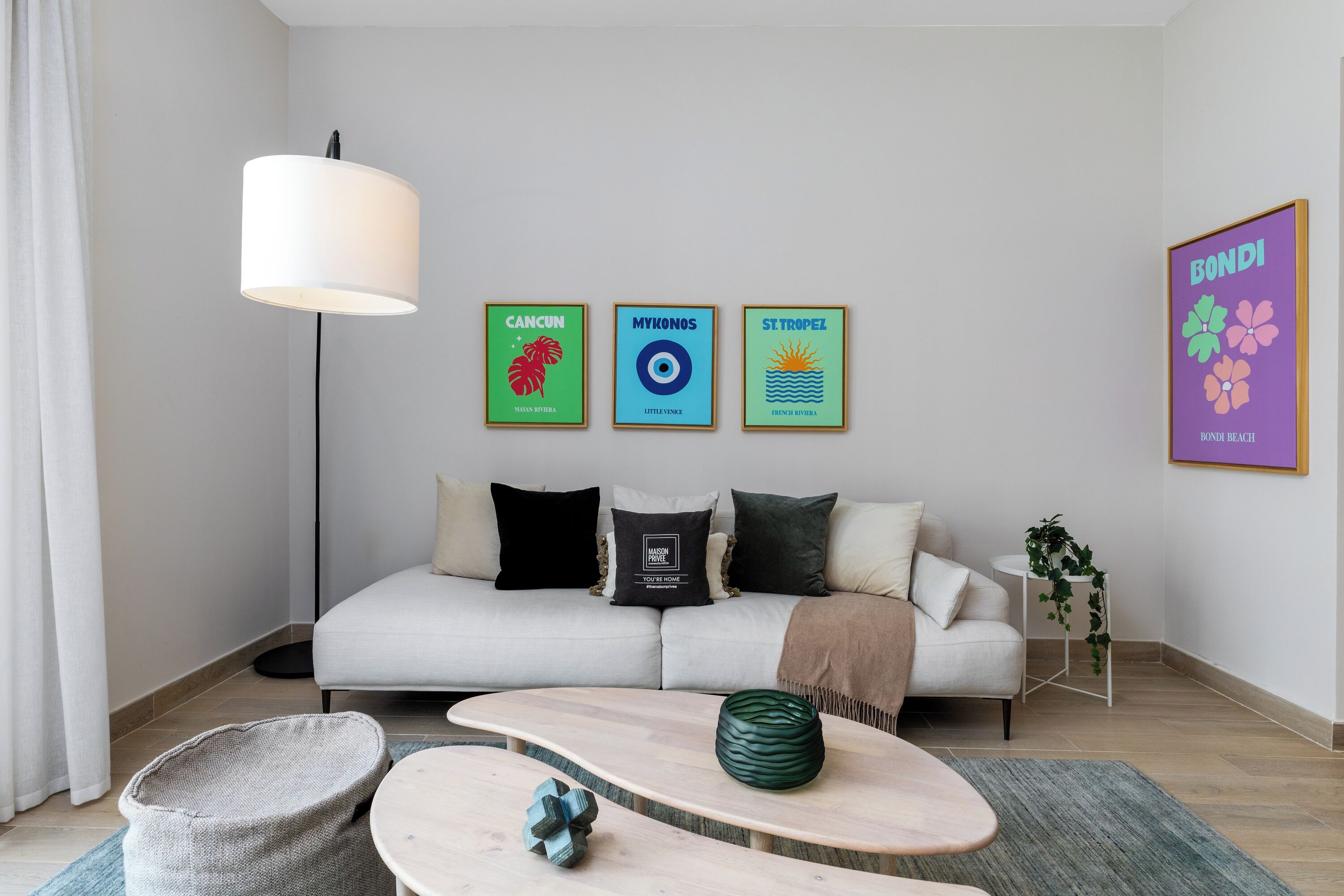 A modern living room with a sofa, a coffee table, and a floor lamp. There are three framed pictures on the wall.