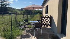 An outdoor patio with a table and chairs, a large umbrella, and a view of a green field and trees.