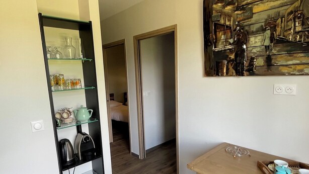 A room with a wooden floor, a glass shelf unit with kitchenware, a painting on the wall, and a table with a tray of cups and a teapot.