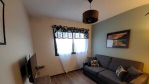 A living room with a sofa, a table, a TV, a window with curtains, and a hanging light fixture.