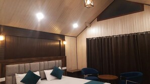 Une chambre d’hôtel avec un grand lit, deux chaises, une petite table et un rideau.