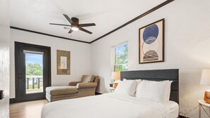 Habitación de hotel con cama, una silla, ventilador de techo, ventana y un cuadro en la pared.
