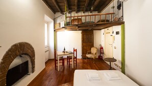 A room with a fireplace, a dining table with chairs, a bed, and a loft area with a wooden railing. - Trastevere Romantic Nest (Roma)
