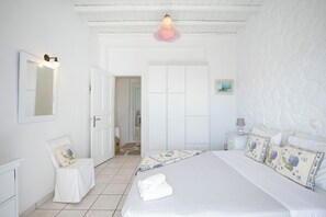 A bedroom with a bed, a bedside table, a nightstand, a mirror, and a door leading to another room.