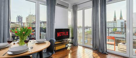 A modern living room with a dining area, large windows, and a view of the cityscape.