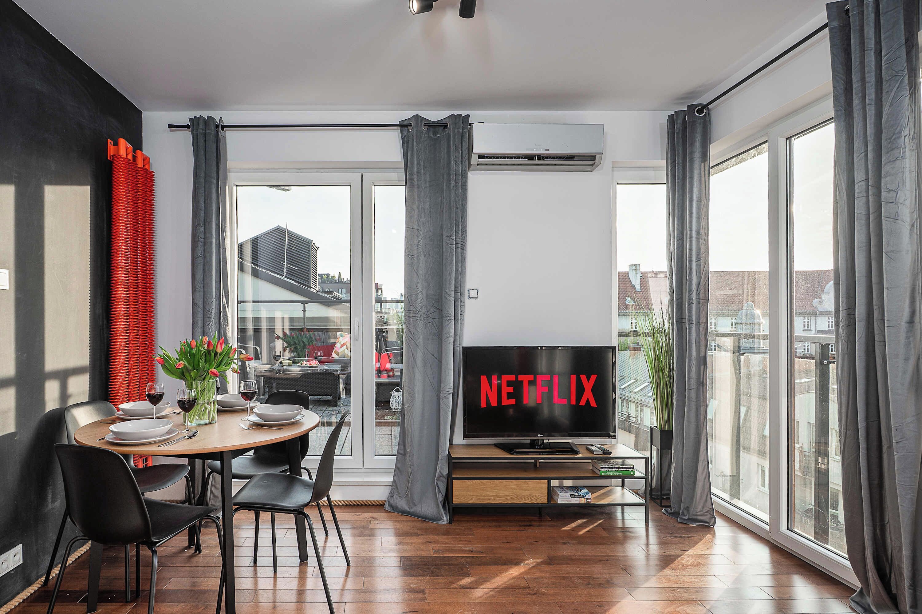 Uma sala de estar moderna com área de refeições, janelas amplas e uma TV exibindo o logotipo da Netflix.