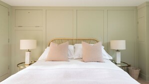 Una cama bien hecha con cabecera de madera, dos lámparas de noche y una cesta de mimbre en el suelo.