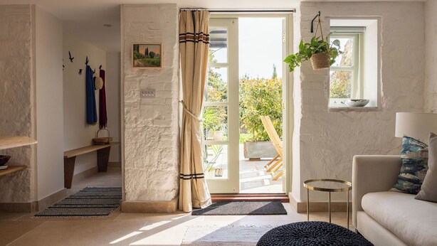 Una sala de estar con sofá, mesa de centro, planta colgante y vistas a través de un ventanal.