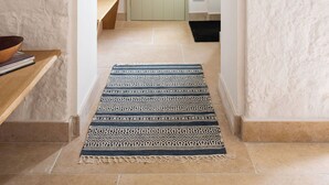 Un pasillo con alfombra estampada, un banco de madera, una cesta y una puerta que da a otra habitación.