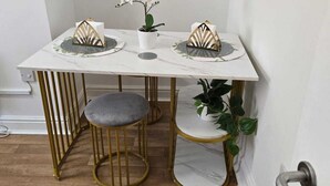 A small dining area with a white table, two gold chairs, a grey stool, and a potted plant. - Luxury Stylish Charming City Apartment With Private Entrance in Wolverhampton (Wolverhampton)