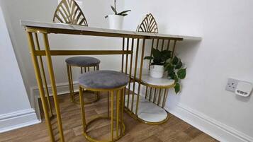 A dining area with a white marble table, gold metal chairs, and a potted plant.