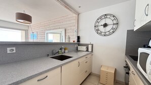 Una cocina moderna con un lavaplatos integrado, un reloj en la pared y una ventana con vista al resto del espacio.